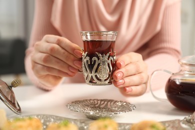 Woman with cup of delicious Turkish tea at white table, closeup