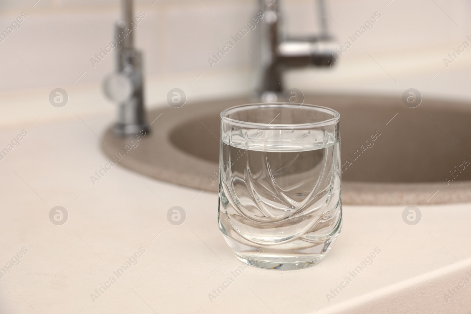 Photo of Glass of water on counter near sink. Space for text