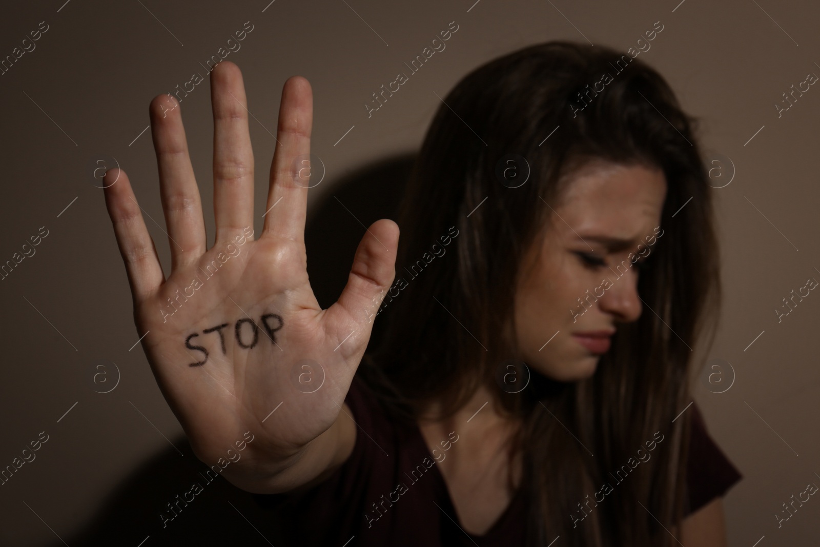 Photo of Abused young woman showing palm with word STOP near beige wall, focus on hand. Domestic violence concept
