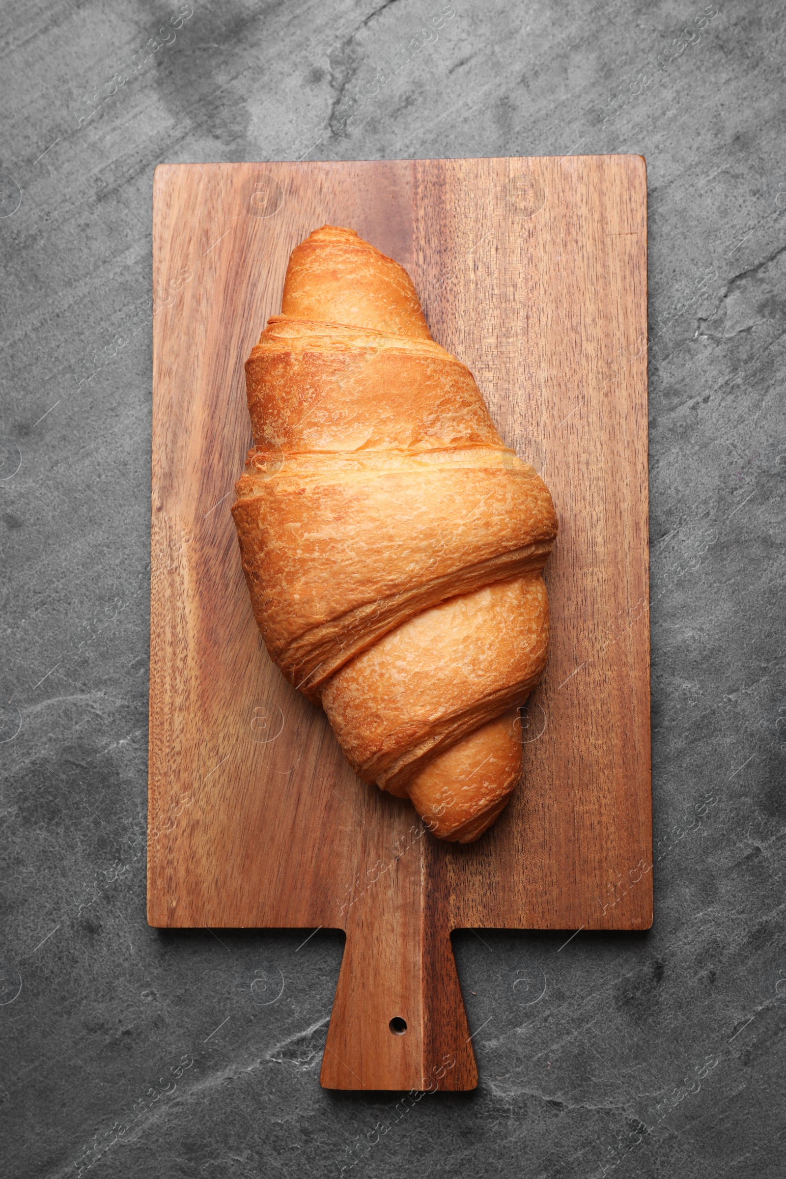 Photo of Tasty fresh croissant on grey table, top view