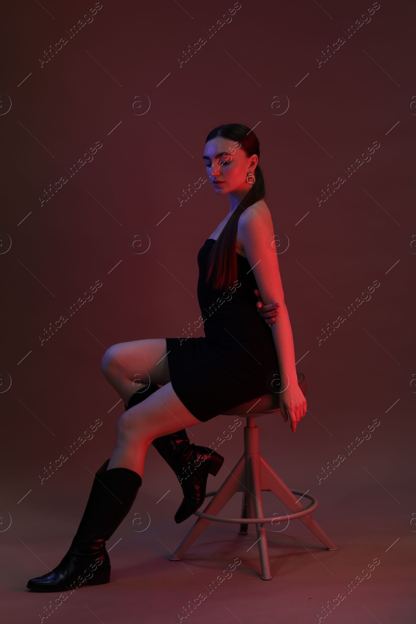 Photo of Beautiful young woman posing on stool against color background in neon lights