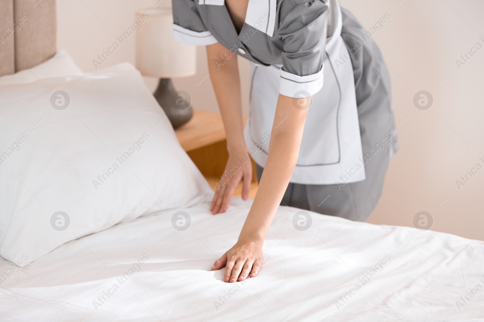 Photo of Young chambermaid making bed in hotel room, closeup