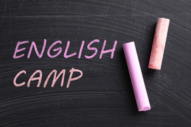 Image of Pieces of color chalk and words ENGLISH CAMP on blackboard, flat lay