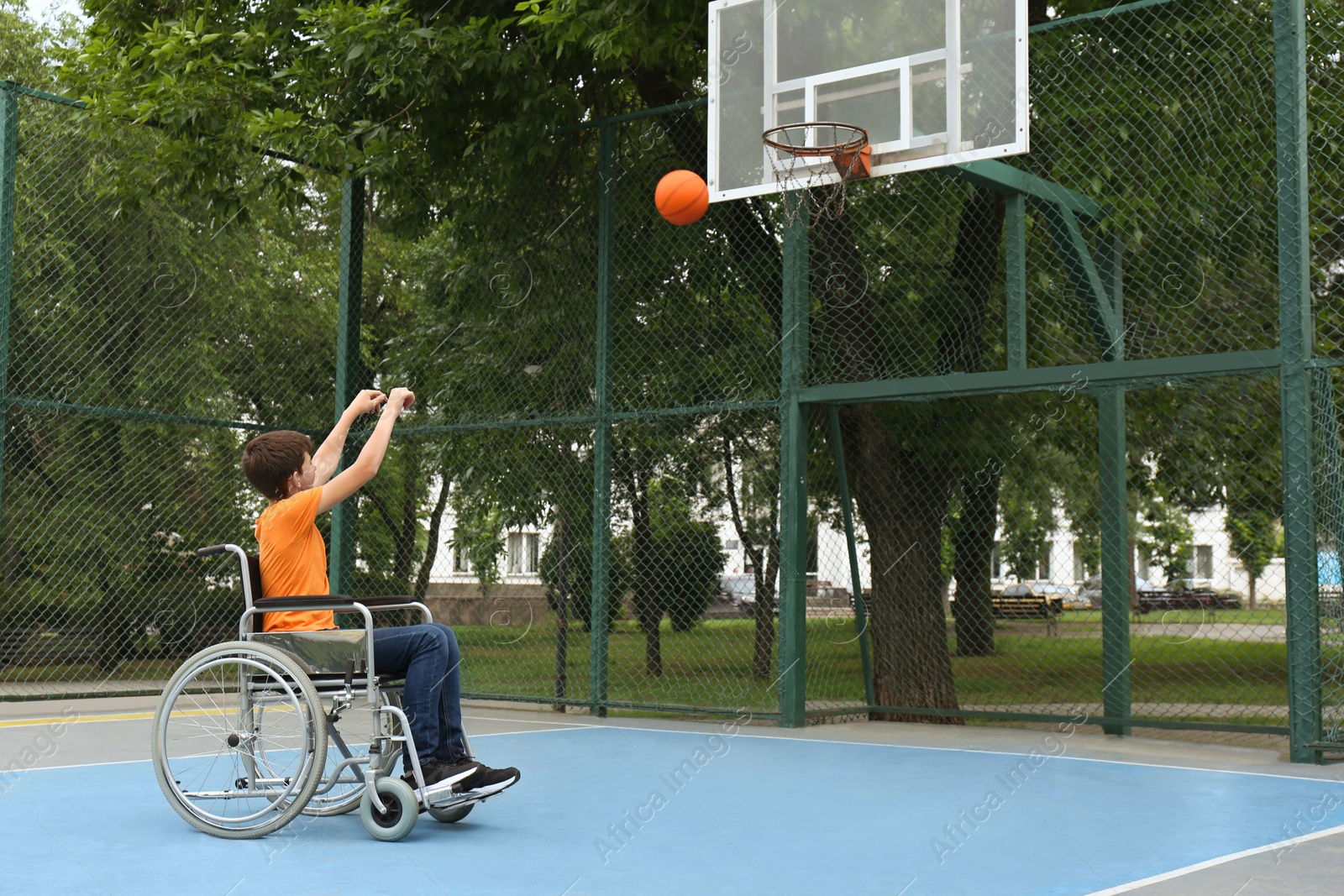 Photo of Disabled teenage boy in wheelchair playing basketball  on outdoor court