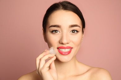 Young woman with ice cube on color background. Skin care