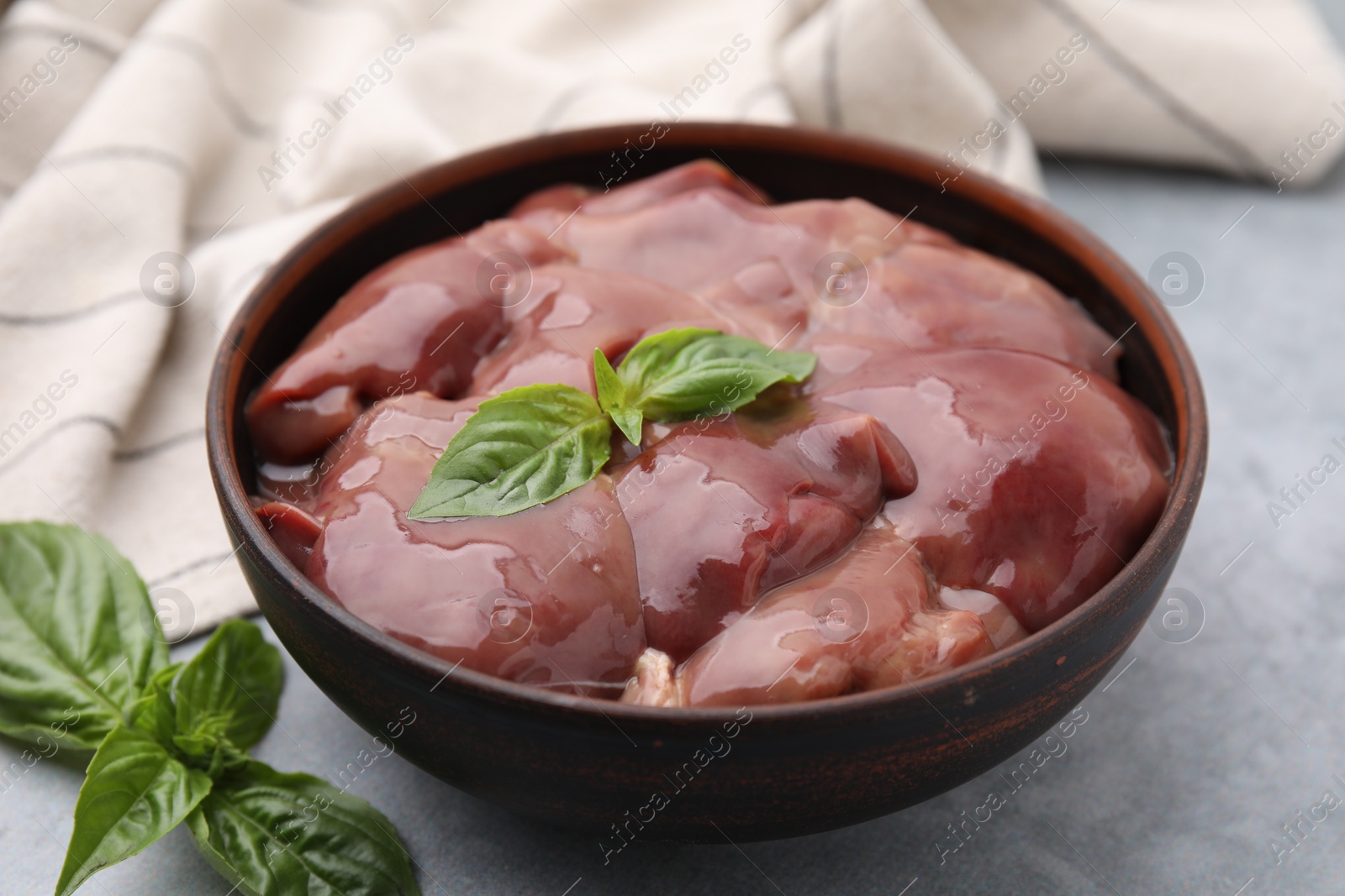 Photo of Bowl with raw chicken liver and basil on light grey table, closeup