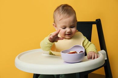 Photo of Cute little baby wearing bib while eating on yellow background