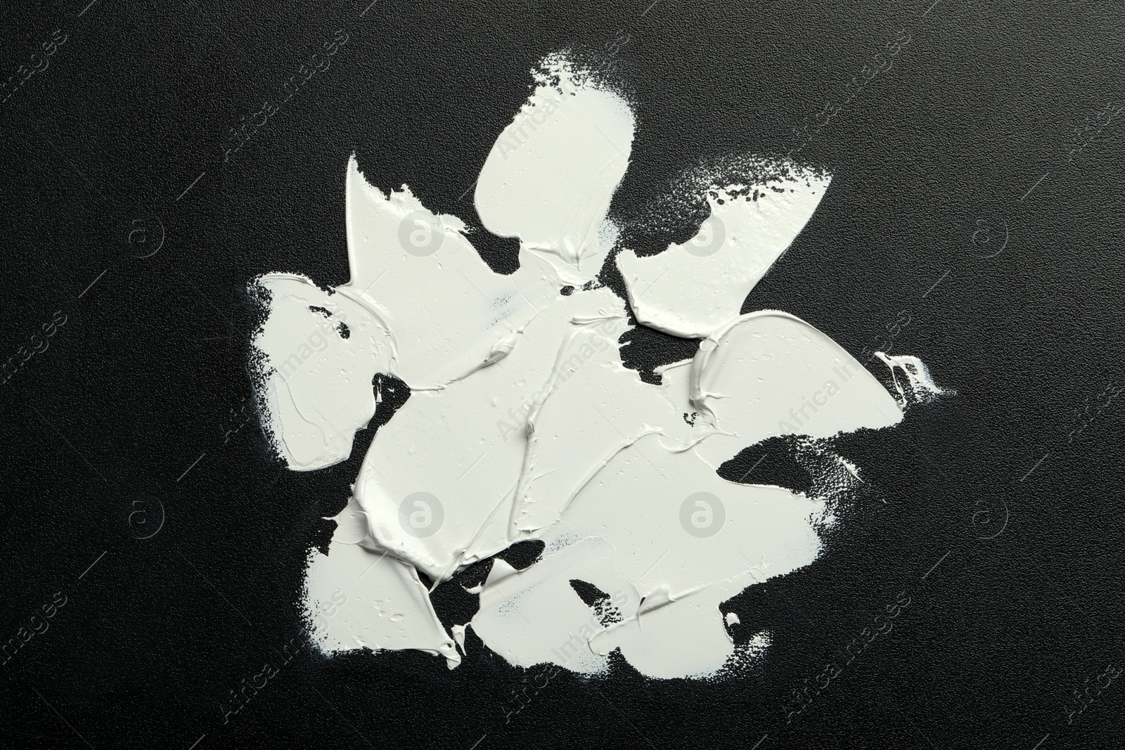 Photo of Strokes of white oil paint on black canvas, top view