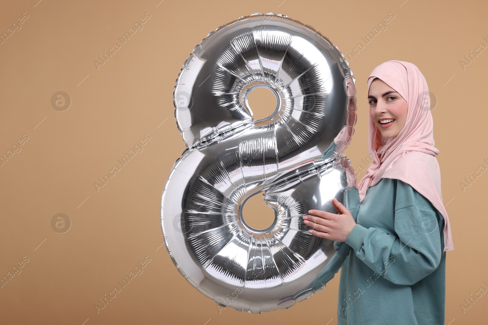 Photo of Happy Women's Day. Woman in hijab with balloon in shape of number 8 on beige background, space for text