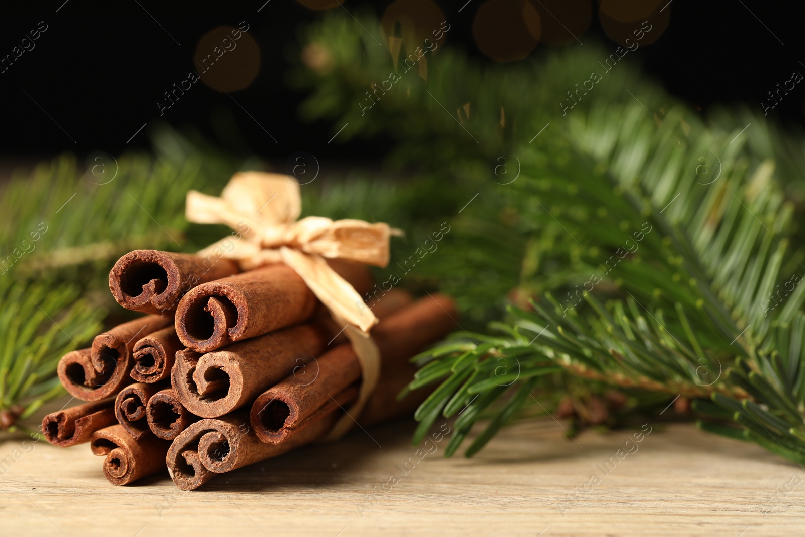 Photo of Bunch of cinnamon sticks and fir branches on wooden table, closeup