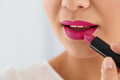 Beautiful woman applying lipstick on light background, closeup