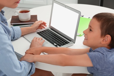 Photo of Little boy bothering mother with laptop at work in kitchen, closeup. Home office concept