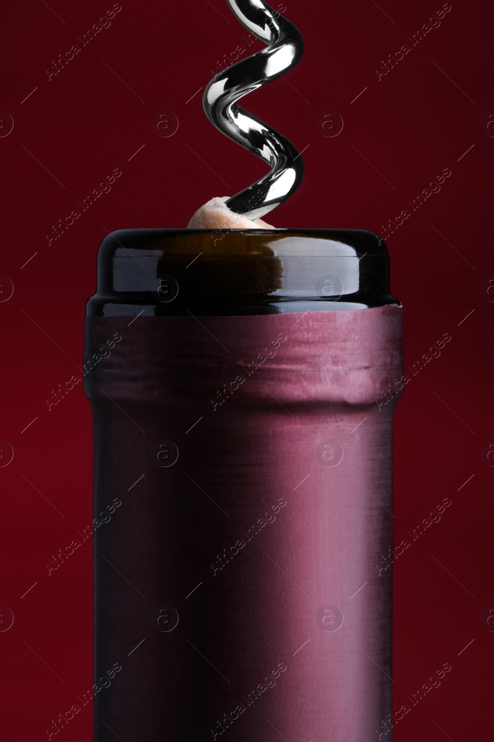 Photo of Opening bottle of wine with corkscrew on burgundy background, closeup