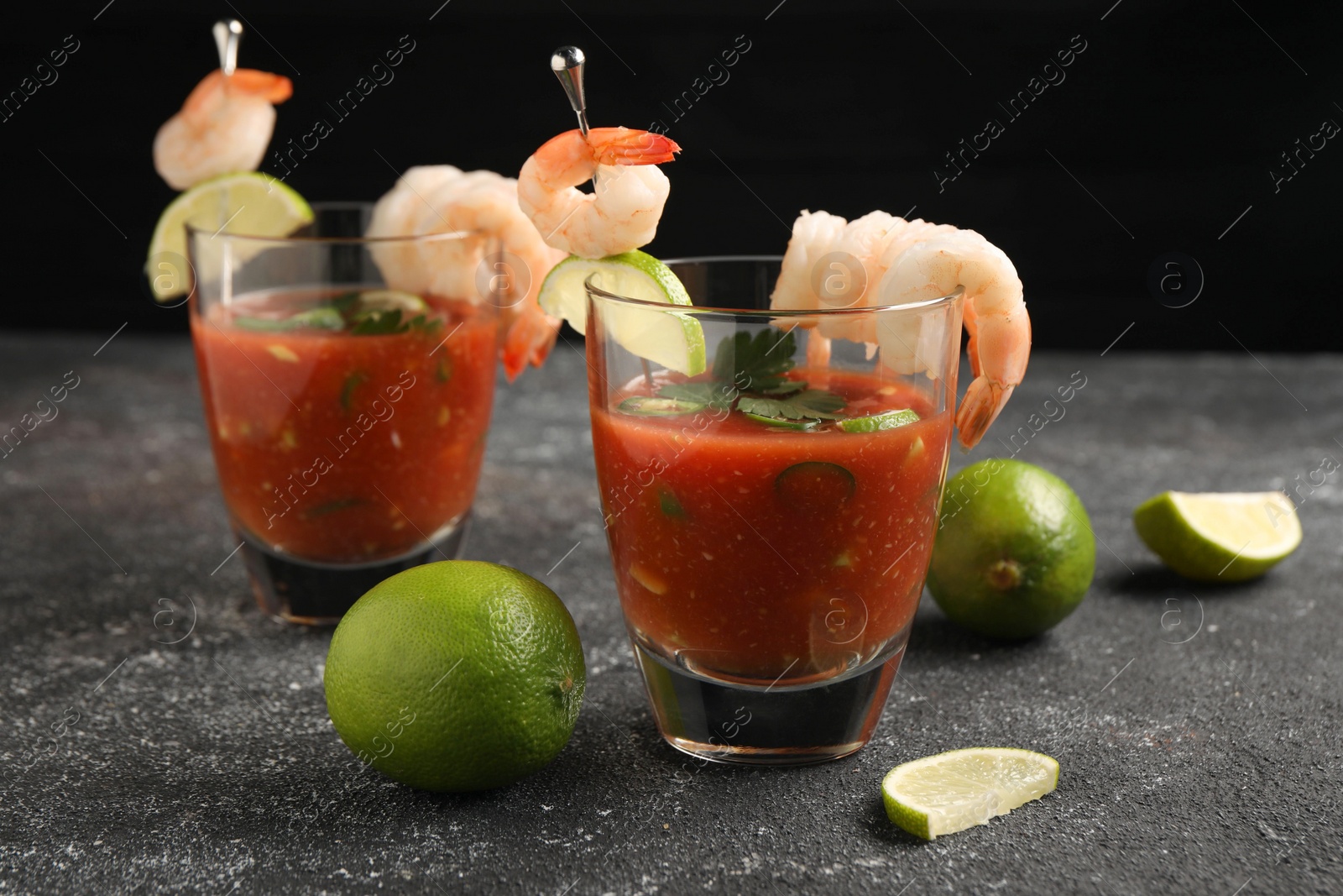 Photo of Tasty shrimp cocktail with sauce in glasses and limes on grey textured table