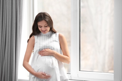 Photo of Beautiful pregnant woman near window at home