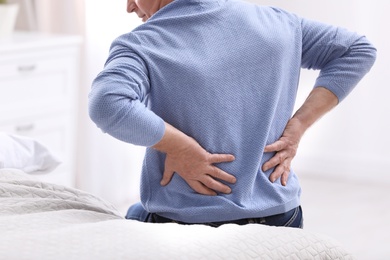 Senior man suffering from back pain at home, closeup