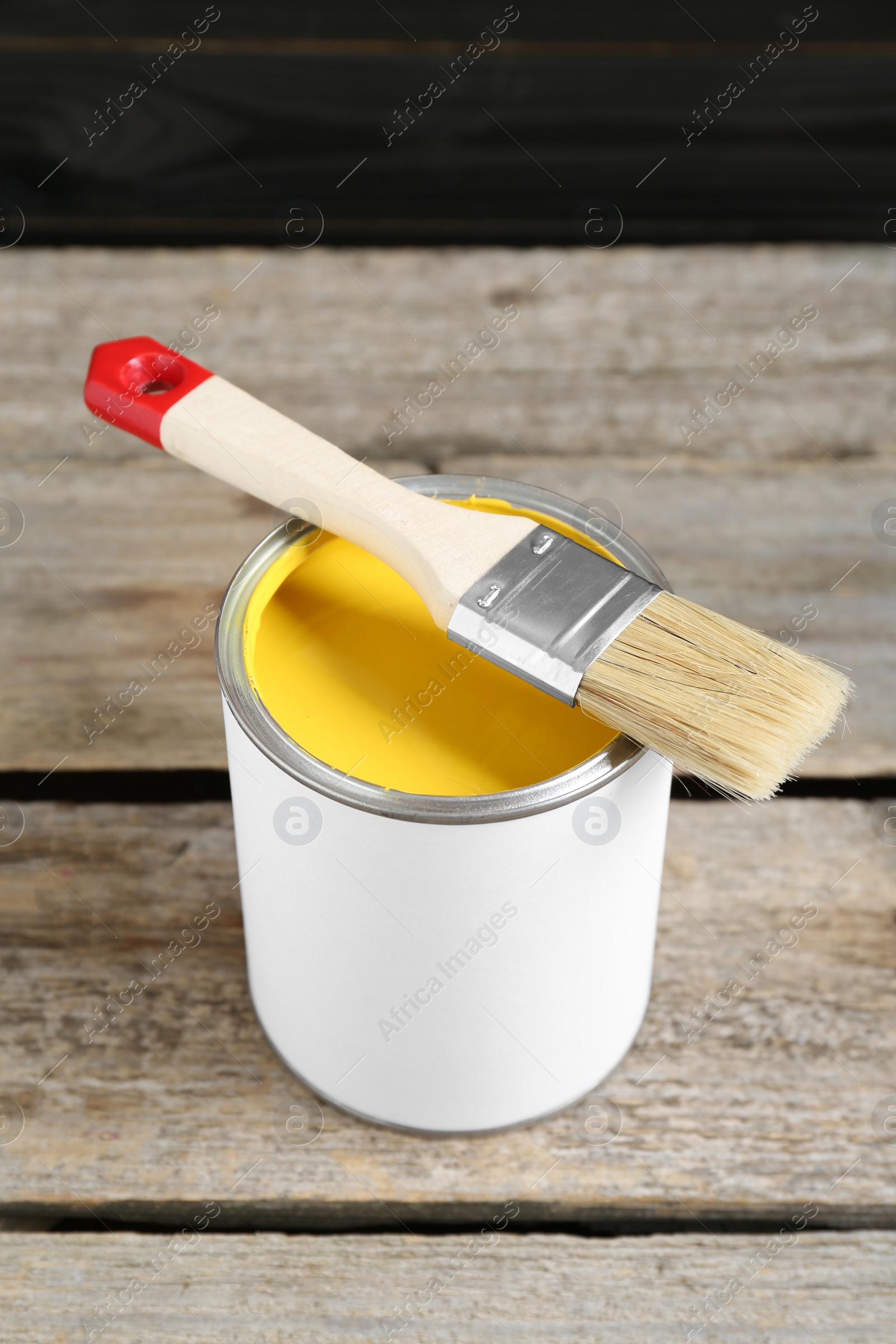 Photo of Can of yellow paint with brush on wooden table