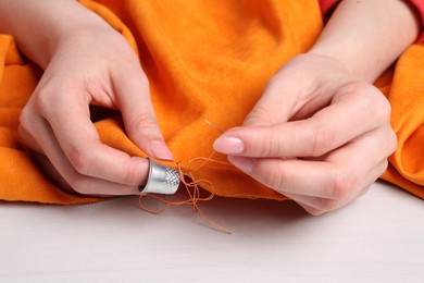 Woman sewing cloth with needle at light wooden table, closeup