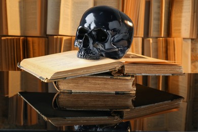 Black human skull and old books on mirror table