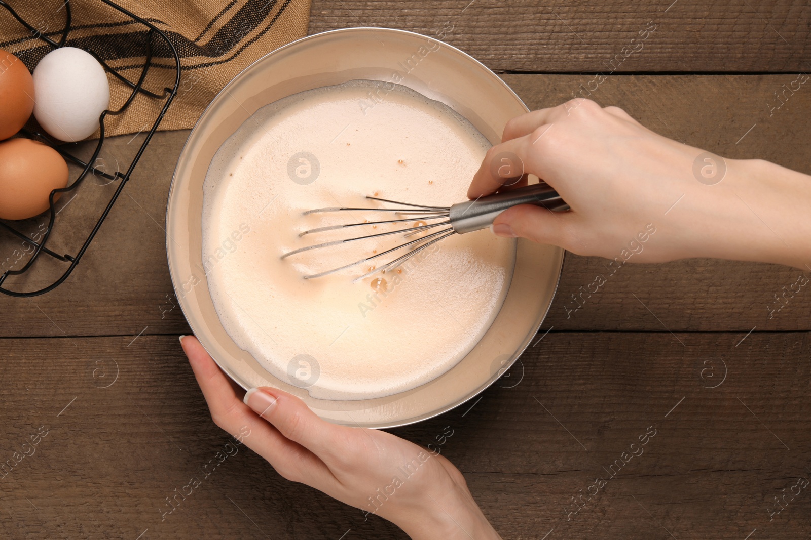 Photo of Woman whipping ingredients with whisk at wooden table, top view. Cooking delicious eggnog