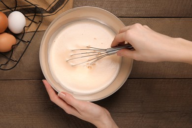 Photo of Woman whipping ingredients with whisk at wooden table, top view. Cooking delicious eggnog