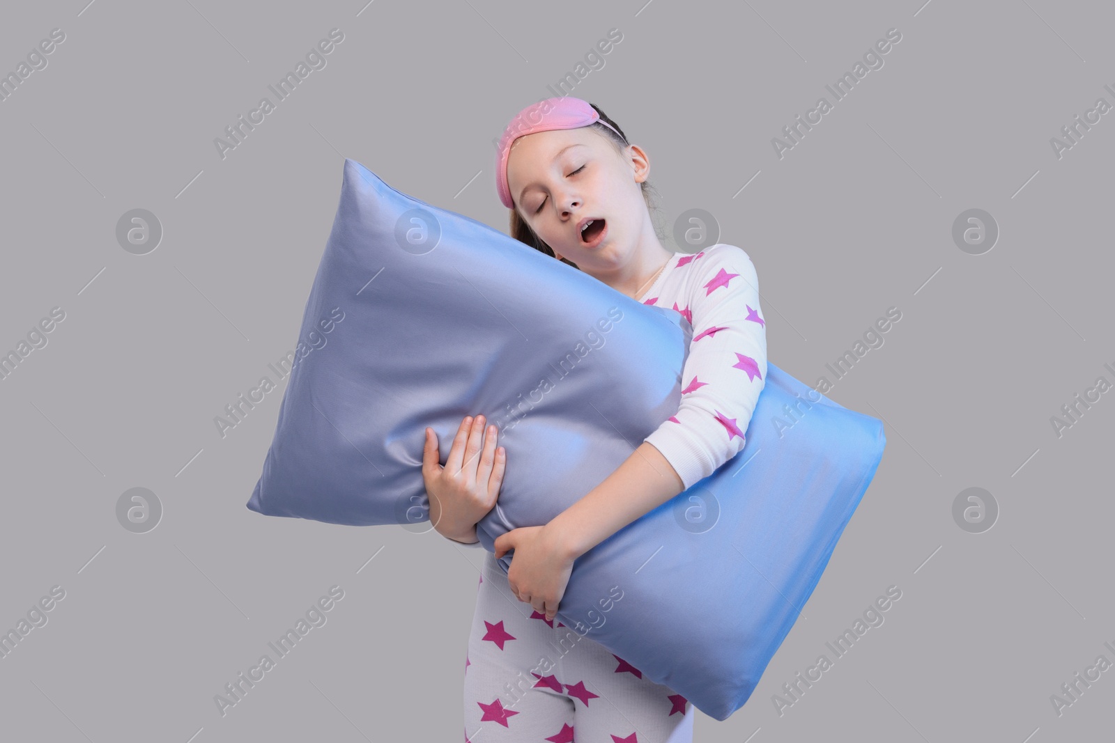 Photo of Girl with sleep mask and pillow yawning on light grey background. Insomnia problem