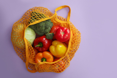 Photo of Net bag with vegetables on lilac background, top view