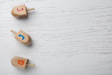 Photo of Hanukkah traditional dreidels with letters Nun, Gimel and Shin on white wooden background, flat lay. Space for text