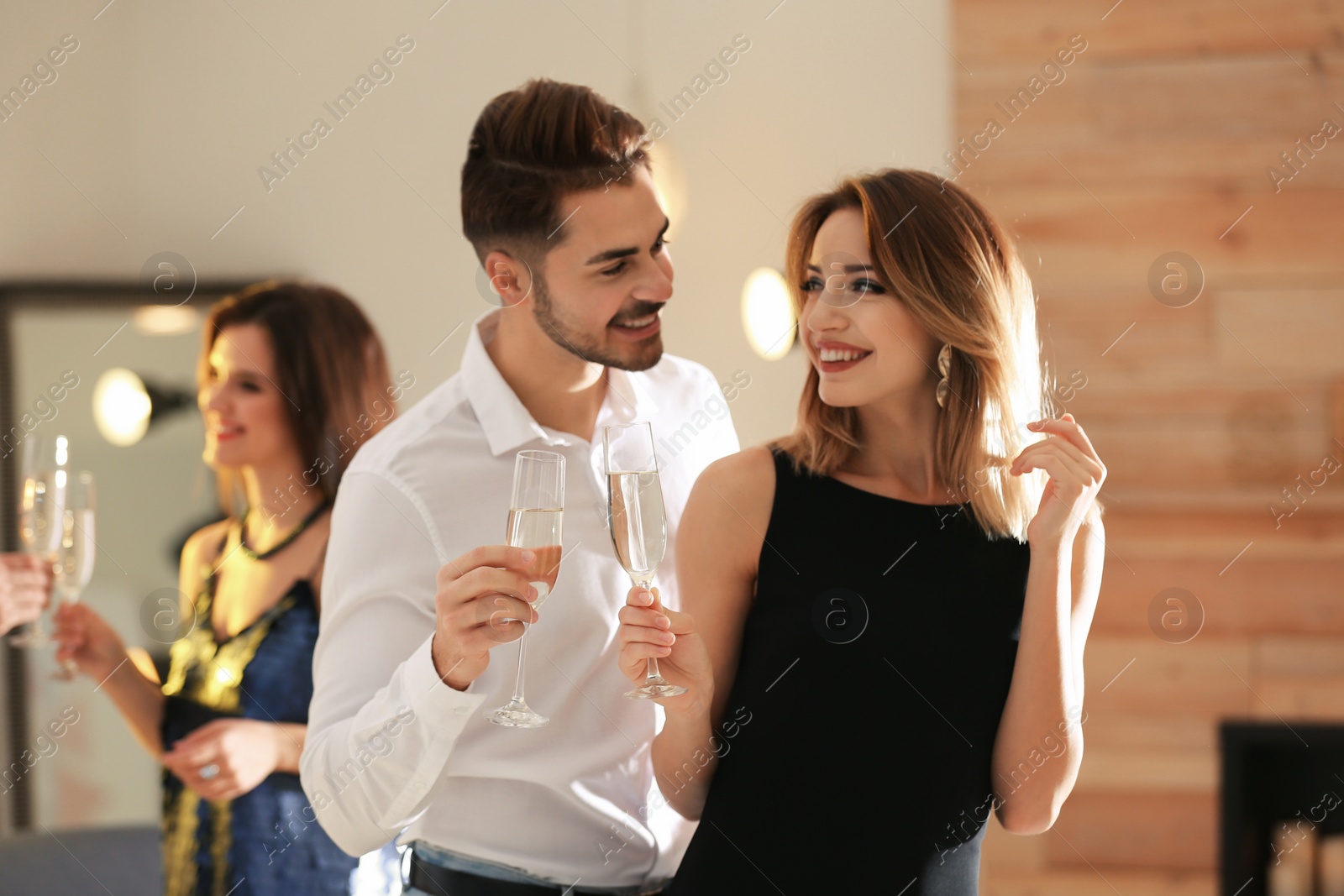 Photo of Happy couple with champagne in glasses having party indoors