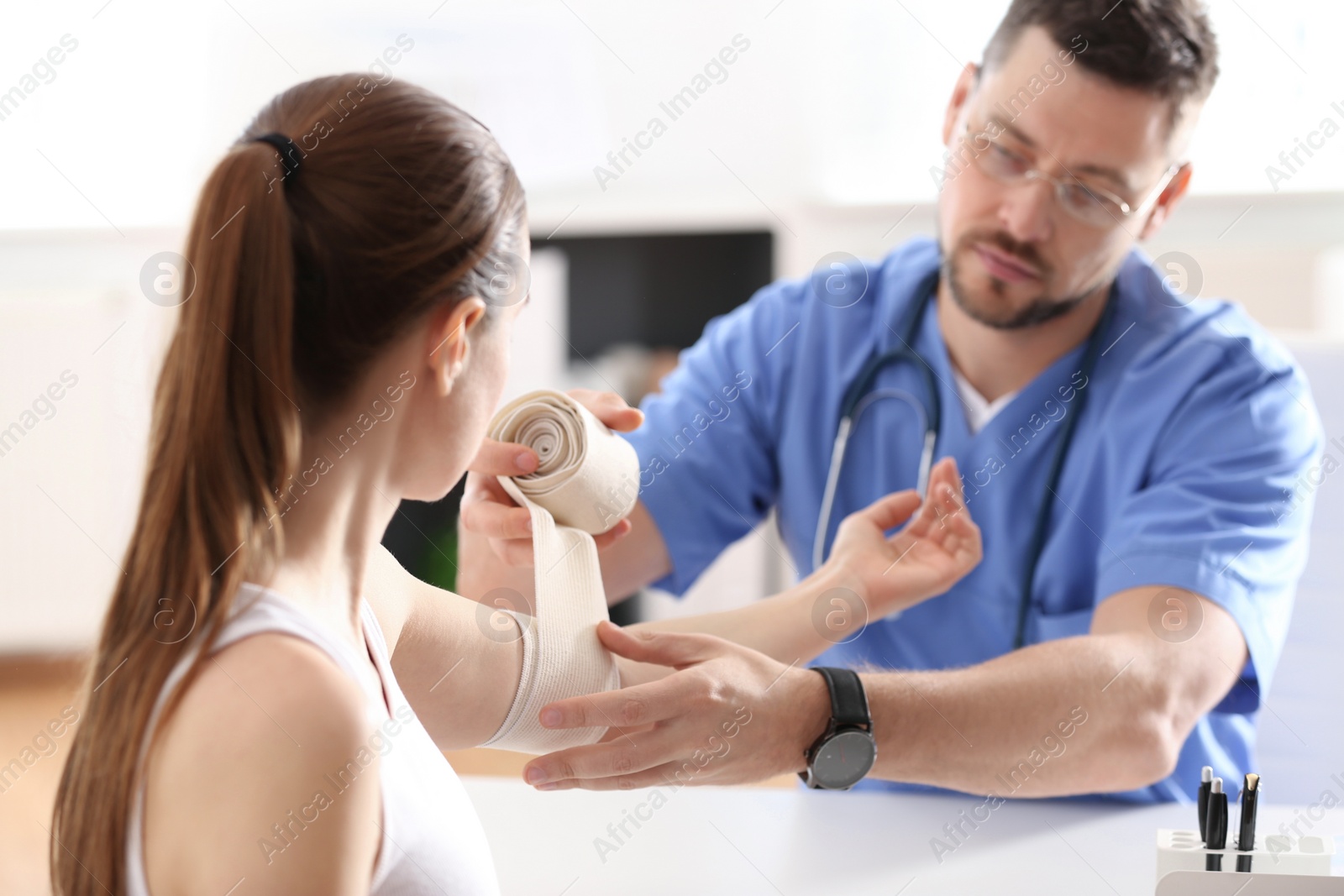 Photo of Male orthopedist applying bandage onto patient's elbow in clinic