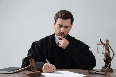 Judge working with documents at wooden table against light grey background