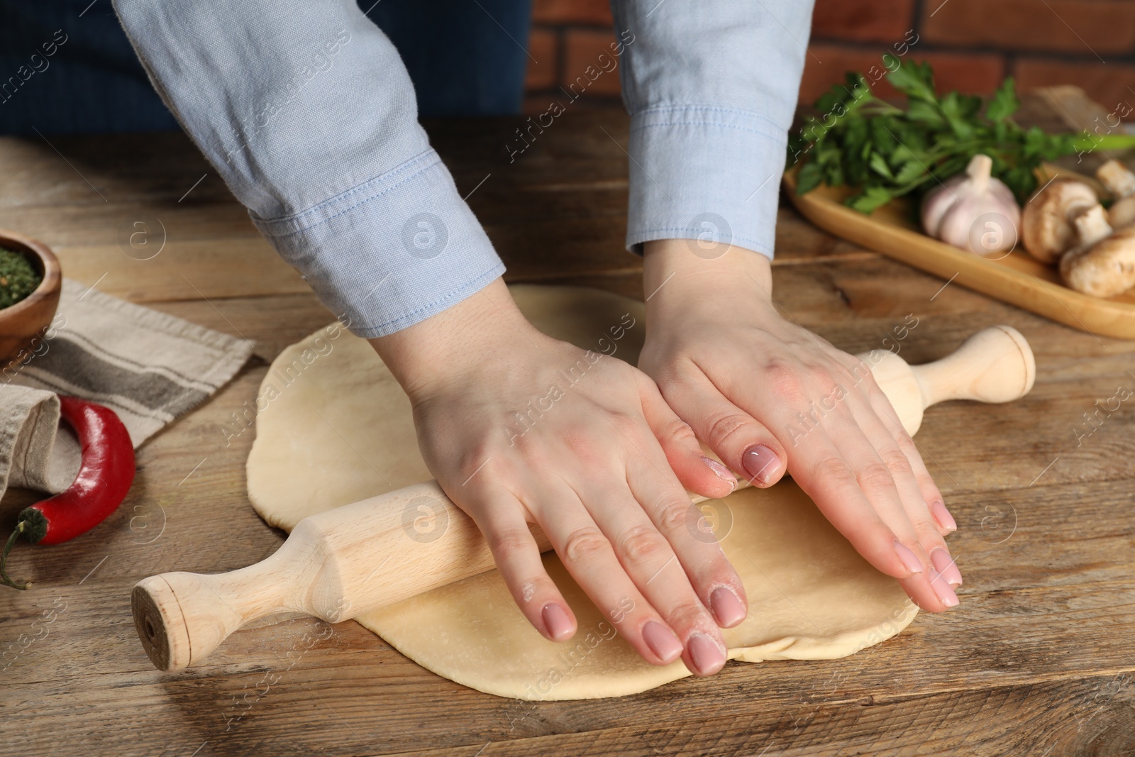 Photo of Woman rolling raw dough at wooden table, closeup