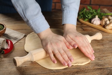 Photo of Woman rolling raw dough at wooden table, closeup