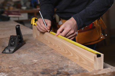Photo of Professional carpenter measuring wooden plank at workbench, closeup