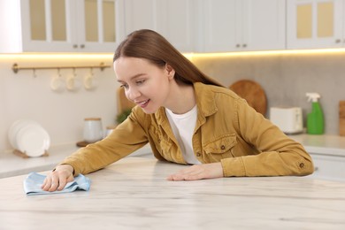 Photo of Woman with microfiber cloth cleaning white marble table in kitchen