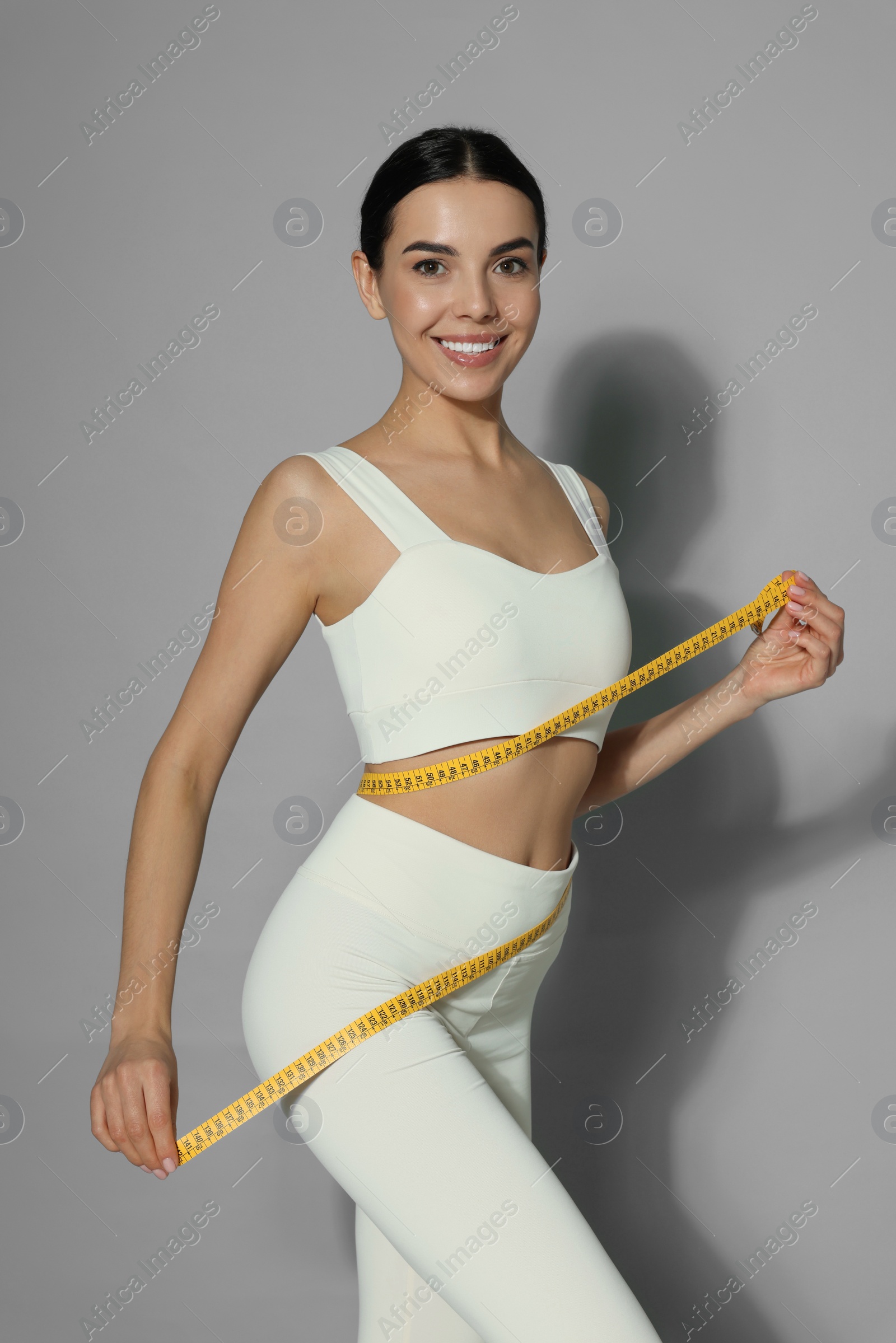 Photo of Young woman measuring waist with tape on grey background