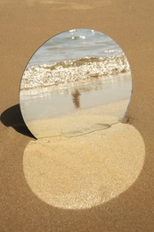 Round mirror reflecting sea on sandy beach