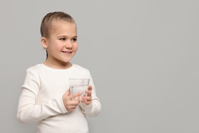 Happy little girl holding glass of fresh water on light grey background, space for text