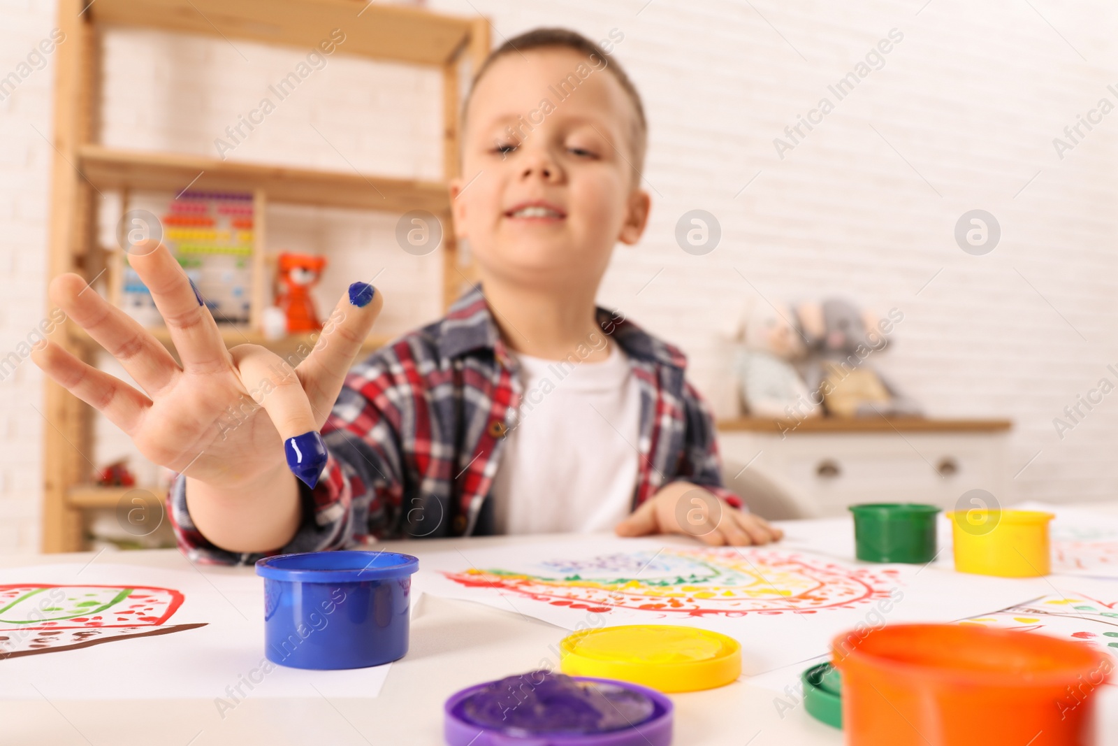 Photo of Little boy painting with finger at white table indoors, focus on hand