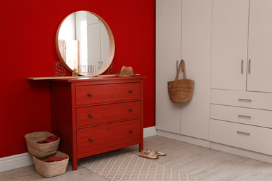 Photo of Round mirror and chest of drawers near red wall in room. Modern interior design