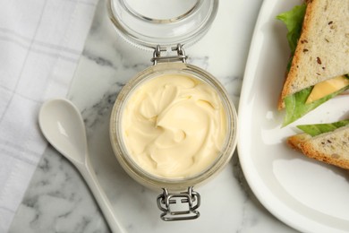 Jar of delicious mayonnaise near fresh sandwiches on white marble table, flat lay