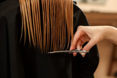 Photo of Professional hairdresser cutting girl's hair in beauty salon, closeup