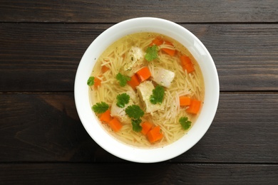 Photo of Dish with fresh homemade chicken soup on wooden background, top view