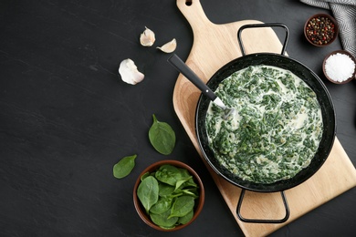 Photo of Tasty spinach dip in frying pan on black table, flat lay. Space for text