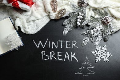 Photo of Flat lay composition of Christmas decorations and white knitted plaid on school blackboard with phrase Winter Break