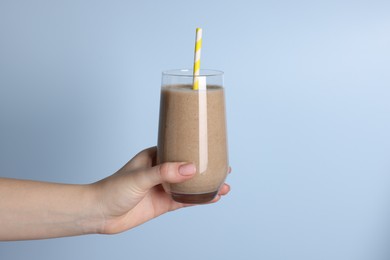 Woman holding glass of tasty smoothie on light blue background, closeup