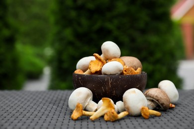 Bowl with different fresh mushrooms on grey rattan table outdoors. Space for text