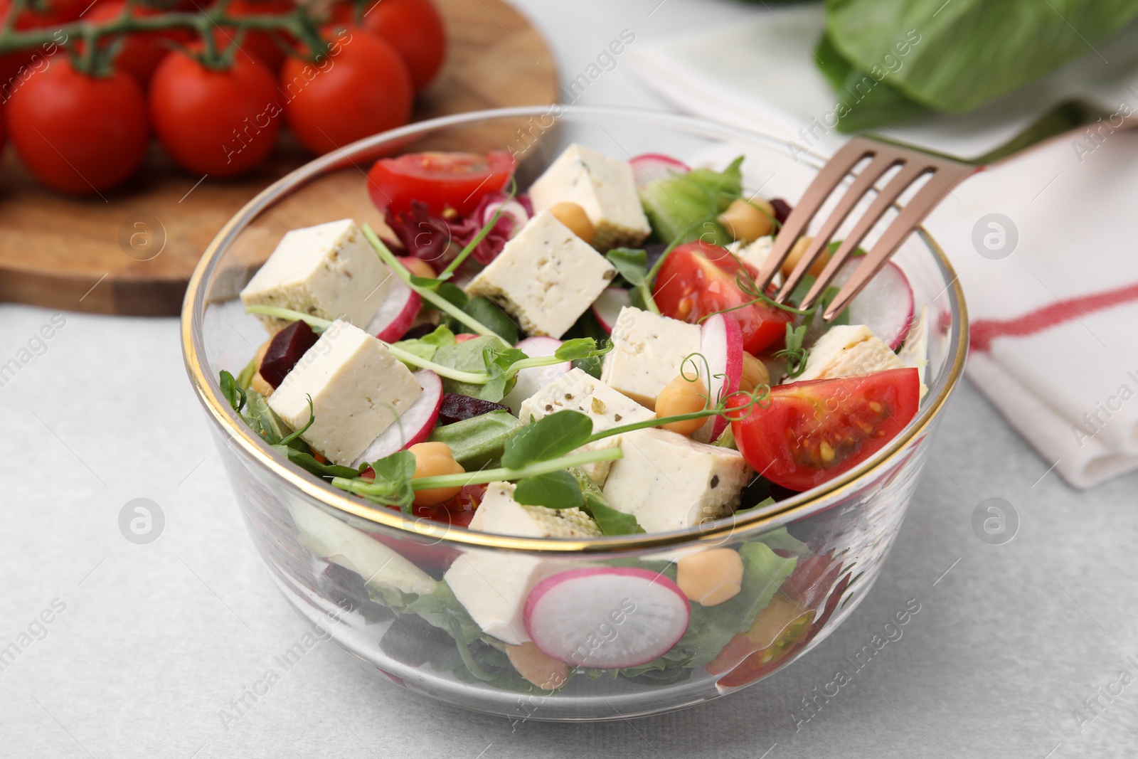 Photo of Bowl of tasty salad with tofu and vegetables on light grey table, closeup