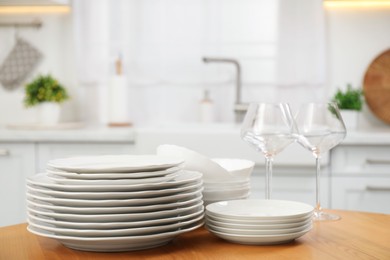 Photo of Clean plates, bowls and glasses on wooden table in kitchen