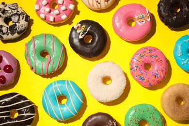 Photo of Different delicious glazed doughnuts on yellow background, flat lay